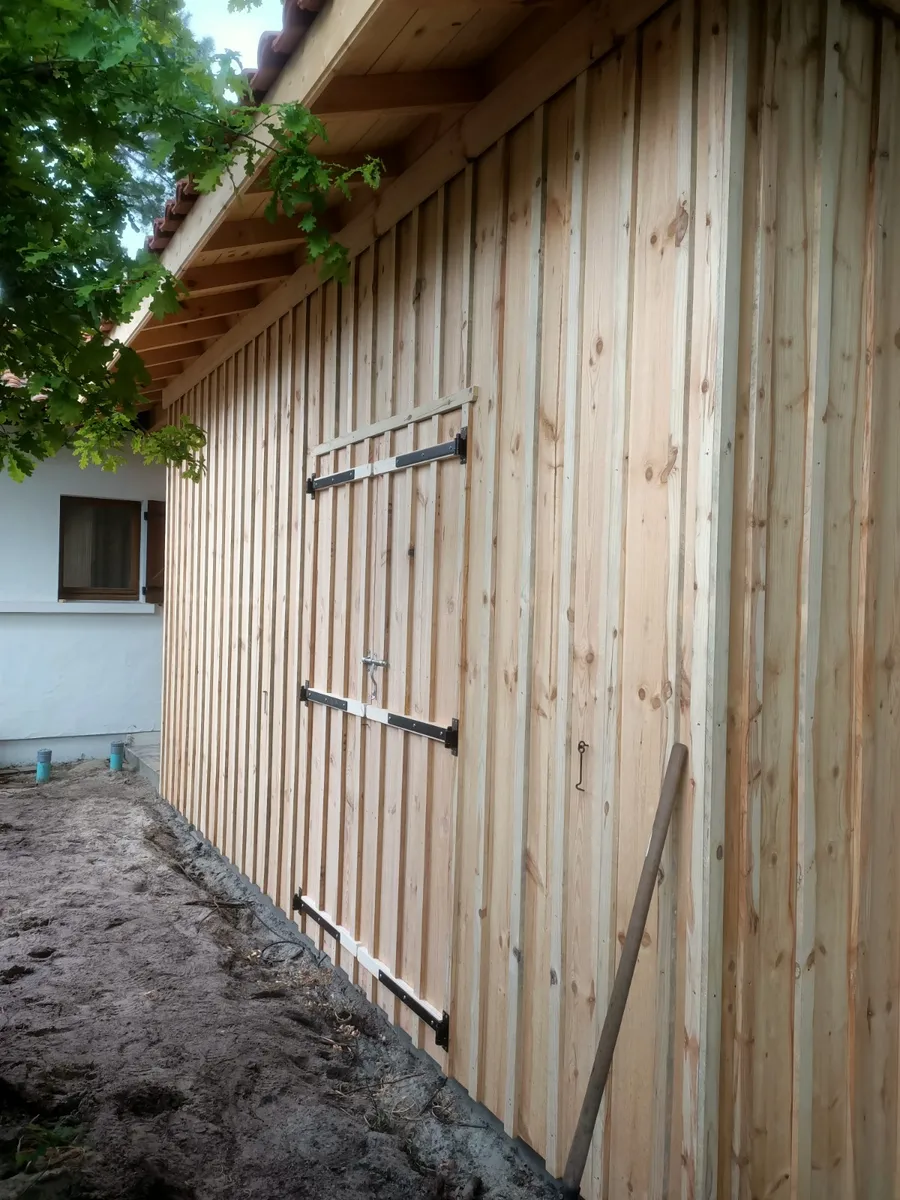 Bâtiment en ossature bois habillé d'un bardage vertical, avec une double porte en bois