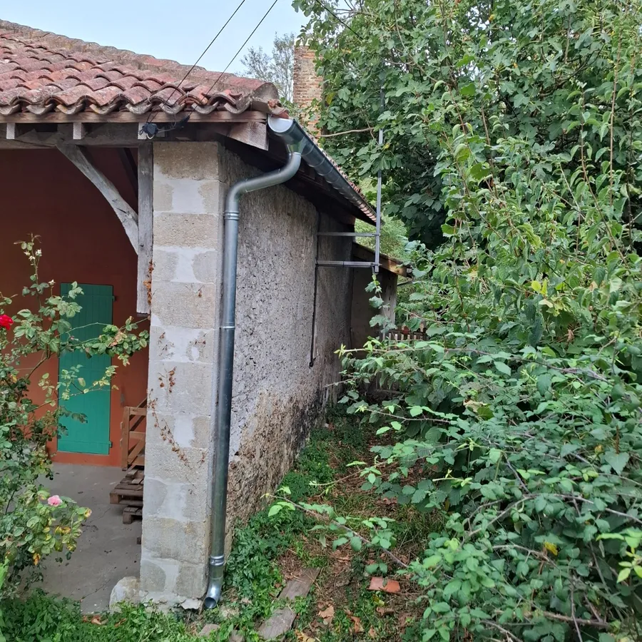 Gouttière et descente en zinc neuves le long d'un mur en pierre